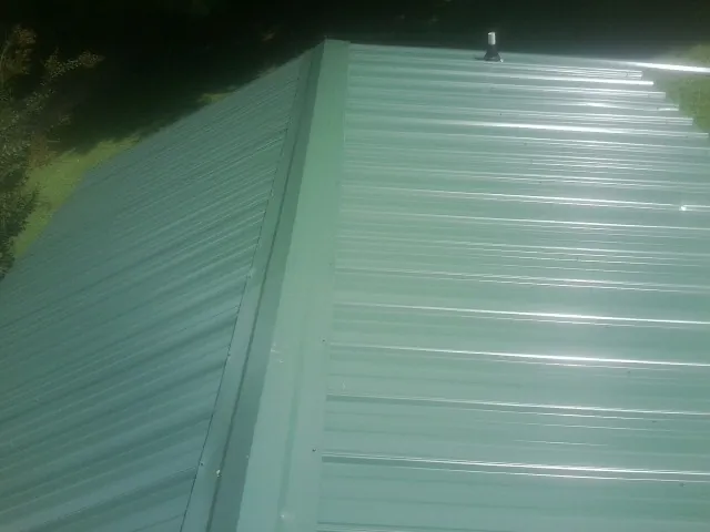 New green metal panels meeting at the ridge of a roof — Flat Roof Repair work by our crew in Pittston