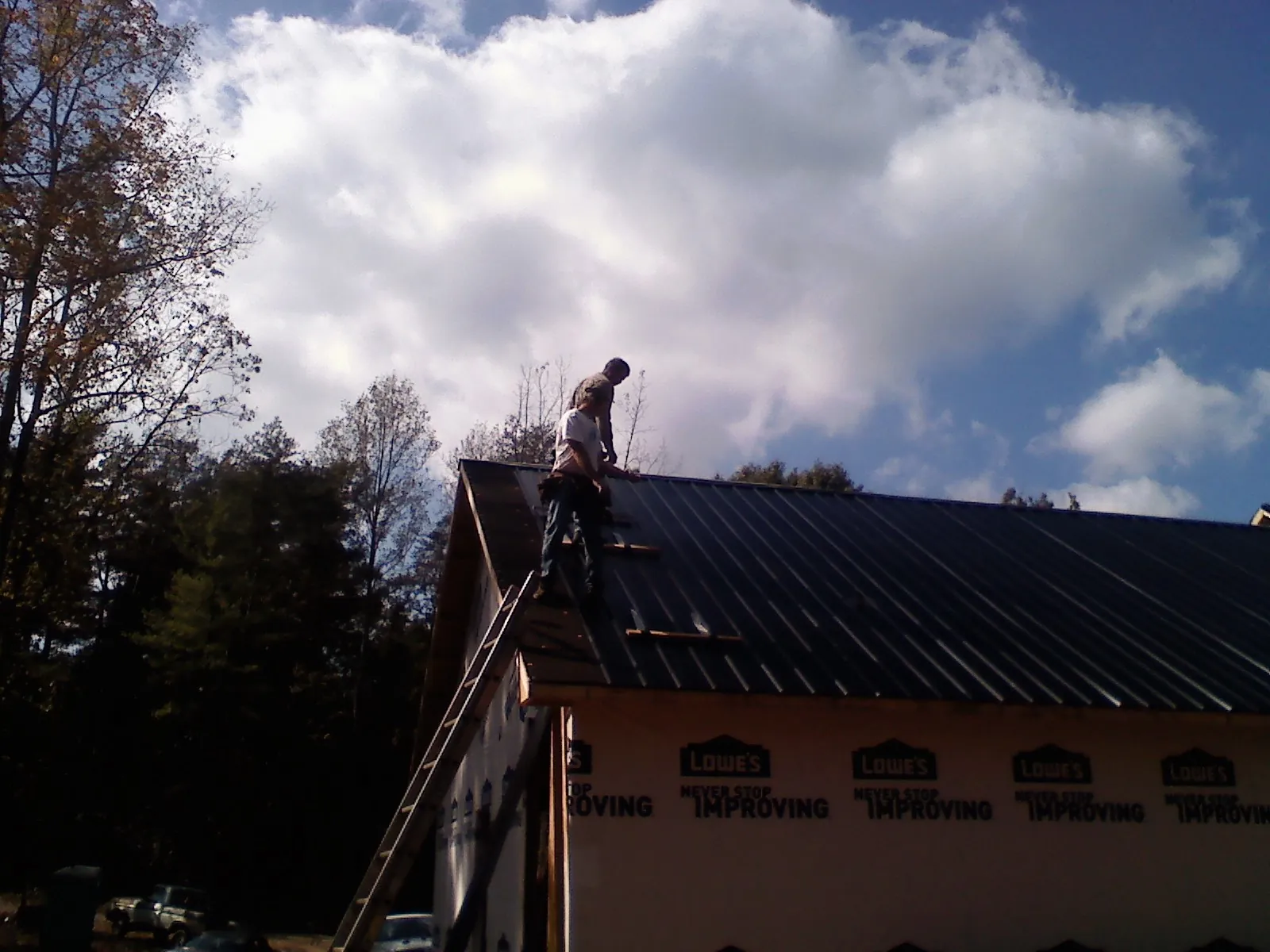 Roofer fastening dark metal panels high against a cloudy sky, from a Roof Inspection job in Pittston