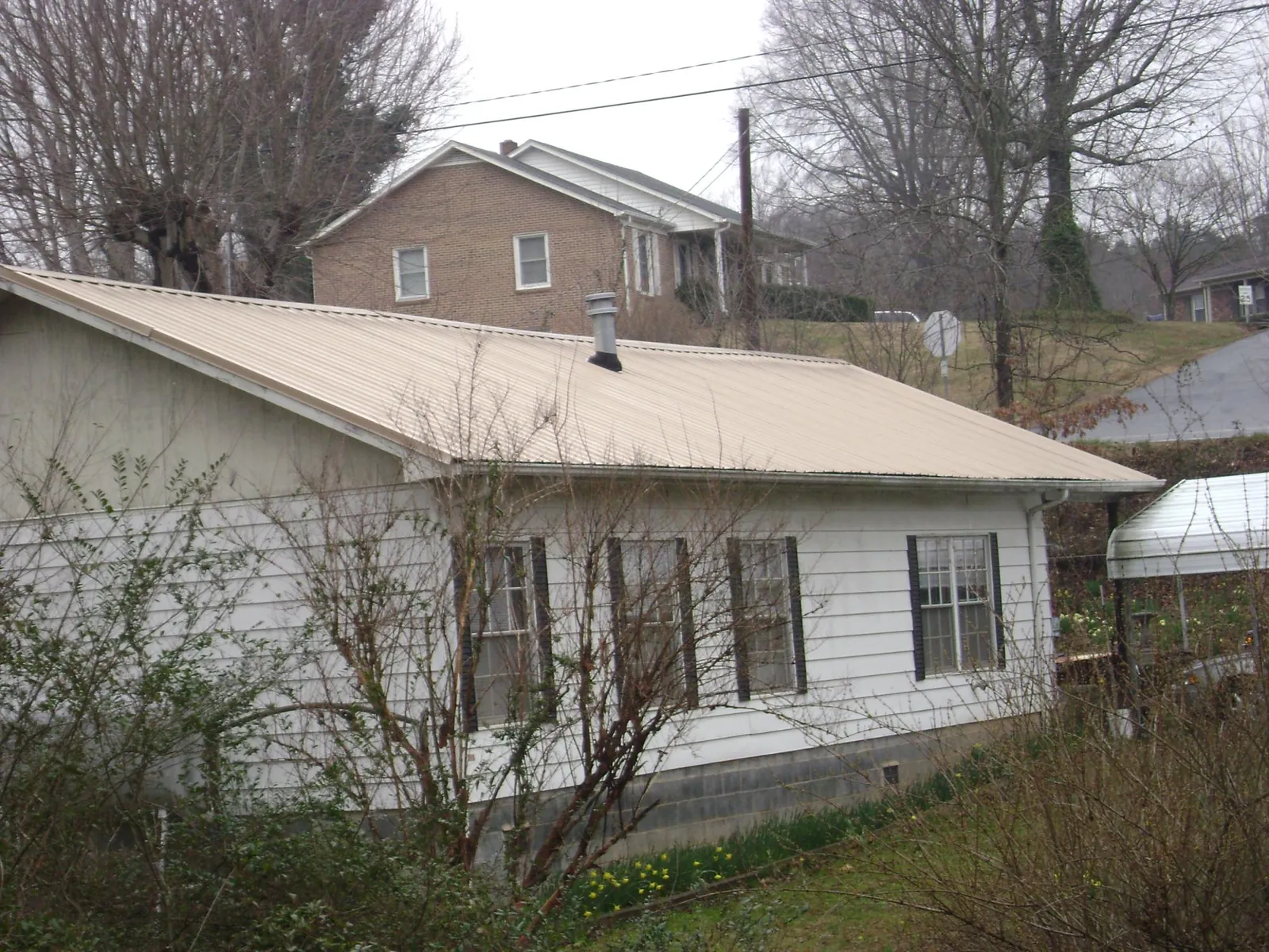 Tan metal roof on a white sided house set into a hillside — Commercial Roofing by Roofing Brothers in Pittston
